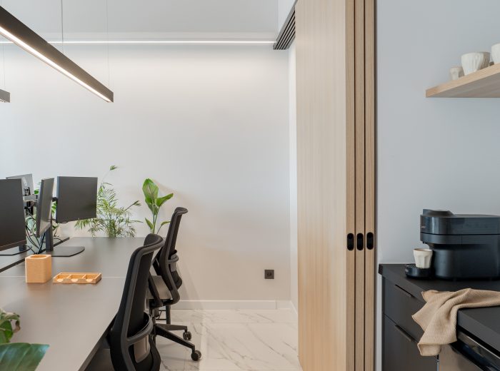 Zona de trabajo de oficina con cuatro puestos, iluminación anti-reflejos y paneles correderos abiertos que revelan almacenamiento e impresora en proyecto AM48, Vitoria-Gasteiz