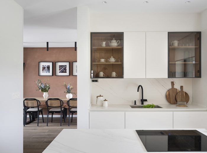 Cocina en blanco con isla central, muebles en blanco con armarios suspendidos puertas cristal, comedor con mesa rectangular sillas en negro y madera y fondo terracota, vivienda unifamiliar LAS, obra nueva y diseño de interiores y amueblamiento, Vitoria-Gasteiz