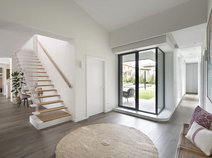 Recibidor acceso a jardín y a piso superior mediante escalera peldaños madera y barandilla tirantes metálicos blanco, vivienda unifamiliar LAS, obra nueva y diseño de interiores, Vitoria-Gasteiz