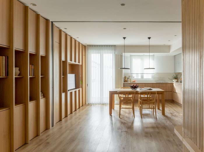 Vista de cocina desde salón con estantería de roble dando continuidad a los espacios mediante cierre acristalado oculto, reforma interior AG76, Vitoria-Gasteiz.