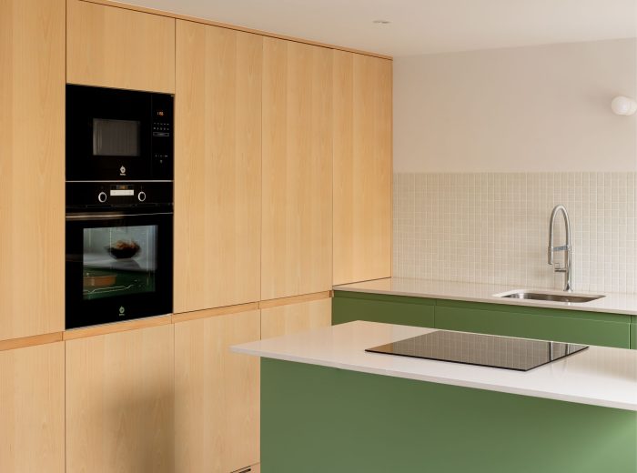 Cocina diseñada a medida con columnas en chapa de haya natural y mobiliario inferior lacado en verde, proyecto O50 en Vitoria-Gasteiz.