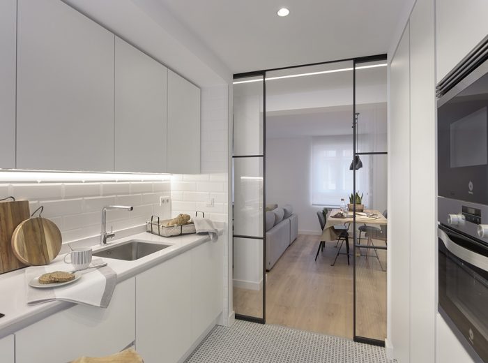 Cocina abierta al espacio de día mediante puertas correderas sincronizadas con perfilería negra, proyecto RB5 en Vitoria-Gasteiz.