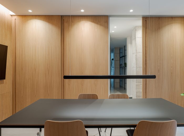 diseño de interiores en sala de reuniones con paneles correderos de madera de roble y paso oculto a la vivienda contigua, optimizando privacidad y funcionalidad en proyecto VG66, Vitoria-Gasteiz
