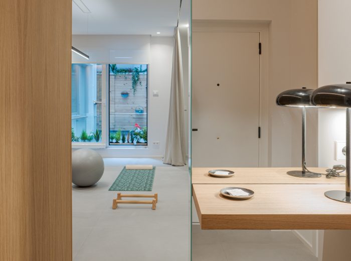 Vista de oficina desde la entrada transformada en sala de ejercicio, con mueble de recibidor a medida y repisa de madera de roble, diseño de interiores multifuncional en proyecto VG66, Vitoria-Gasteiz