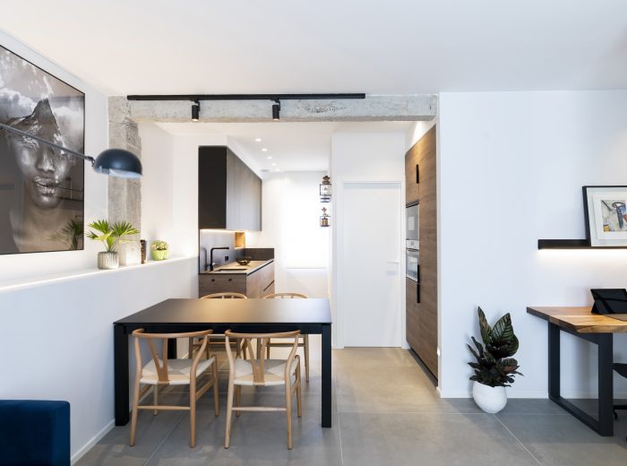 Cocina-comedor abierta a medida que optimiza el espacio, con mobiliario negro y mesa integrada que refuerzan la continuidad visual, reforma integral ZB4 en Vitoria-Gasteiz.